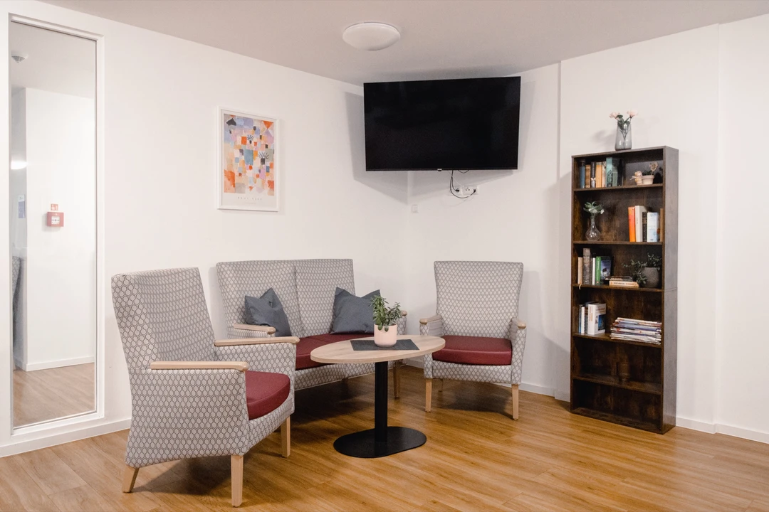 Aufenthaltsraum mit Polstersesseln, Bücherregal und Fernseher