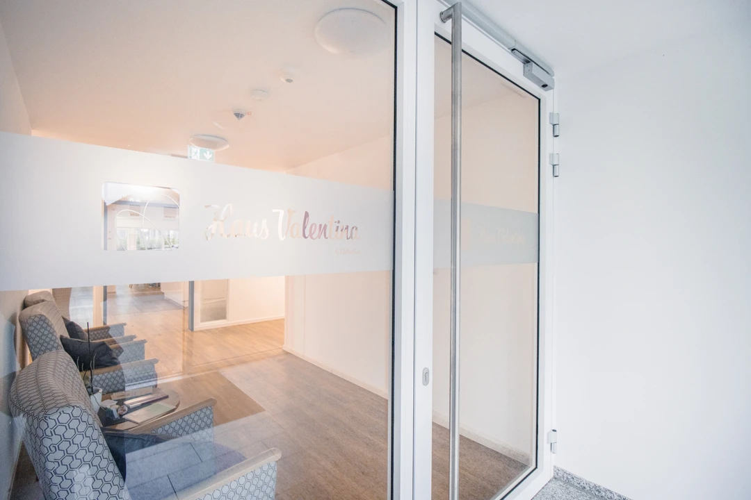 Blick durch die Glastür in den Empfangsbereich des Haus Valentina mit Sesseln