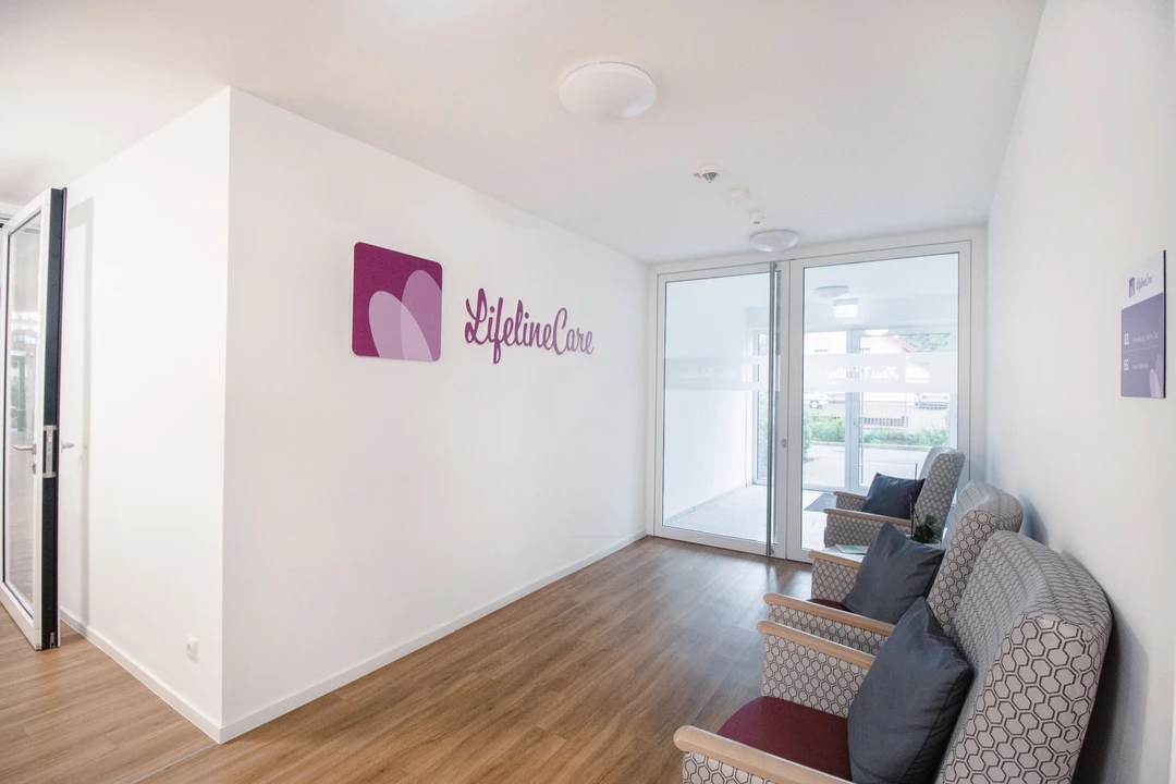 Empfangsbereich mit dem Lifeline-Care-Logo an der Wand und Sesseln am Fenster