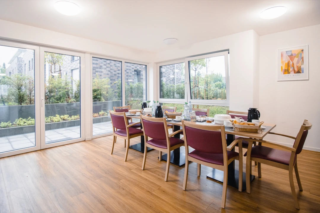 Gemeinschaftsraum mit gedecktem Tisch und bodentiefen Fenstern zur Terrasse