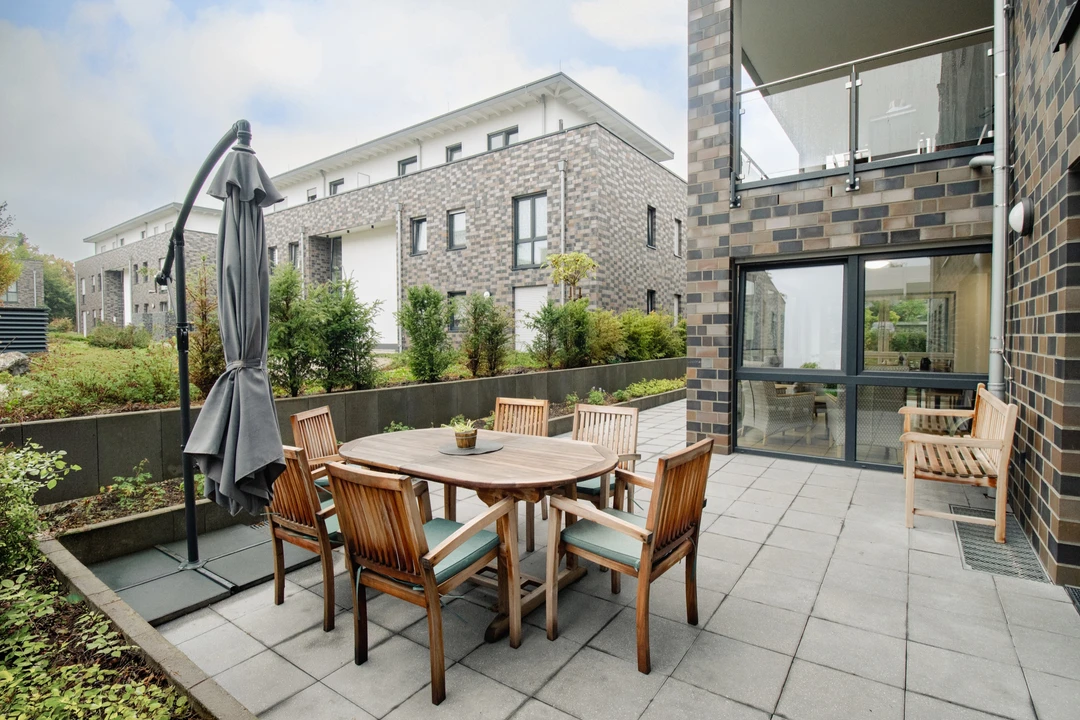 Terrasse mit Gartenmöbeln, Sonnenschirm und bepflanzten Beeten