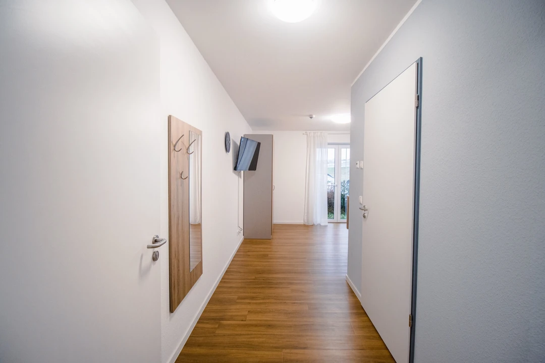 Eingangsbereich eines Zimmers mit Garderobe, Spiegel und Blick in den Wohnbereich